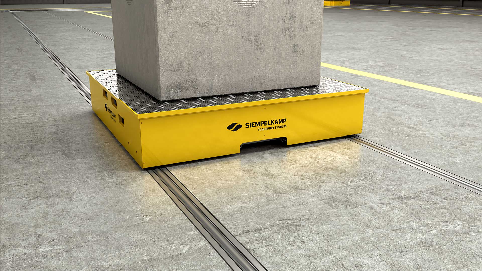 Ein gelbes Transportgerät mit einem Betonblock darauf, platziert auf einem Industrieboden mit eingelegten Schienen.