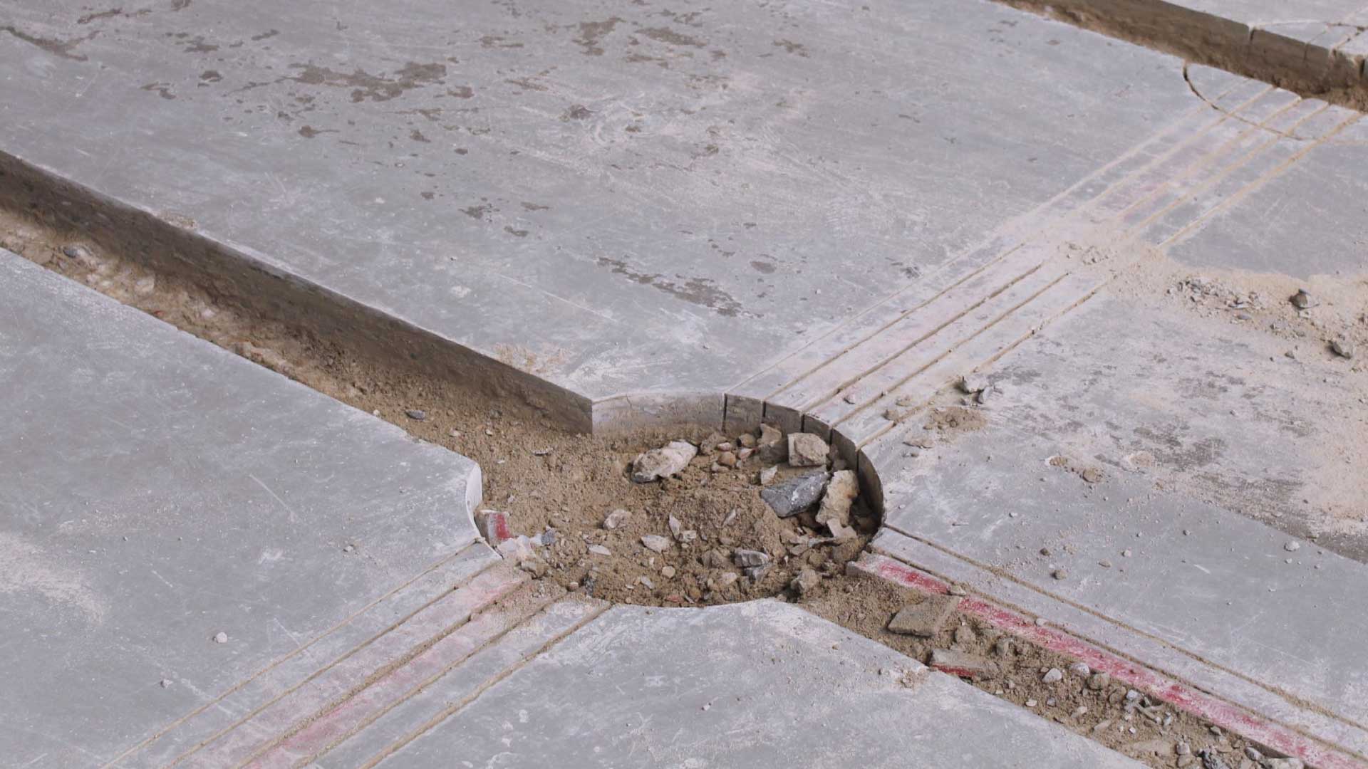 Ein Ausschnitt eines Betonbodens mit einer kreisförmigen Vertiefung, umgeben von Erde und Gestein.