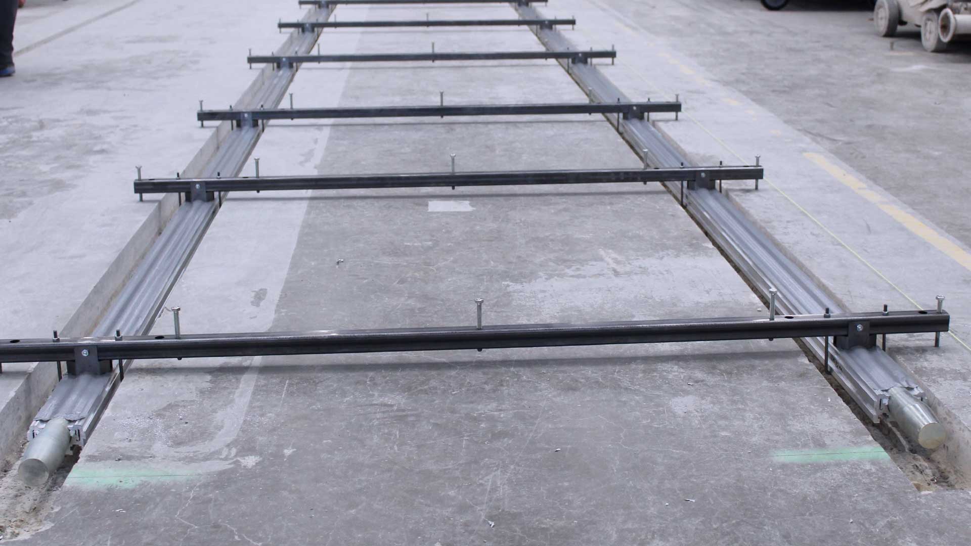 Eine Reihe von Metallprofilen, die auf einem Betonboden verlegt sind, vermutlich als Schiene oder Trägerkonstruktion.