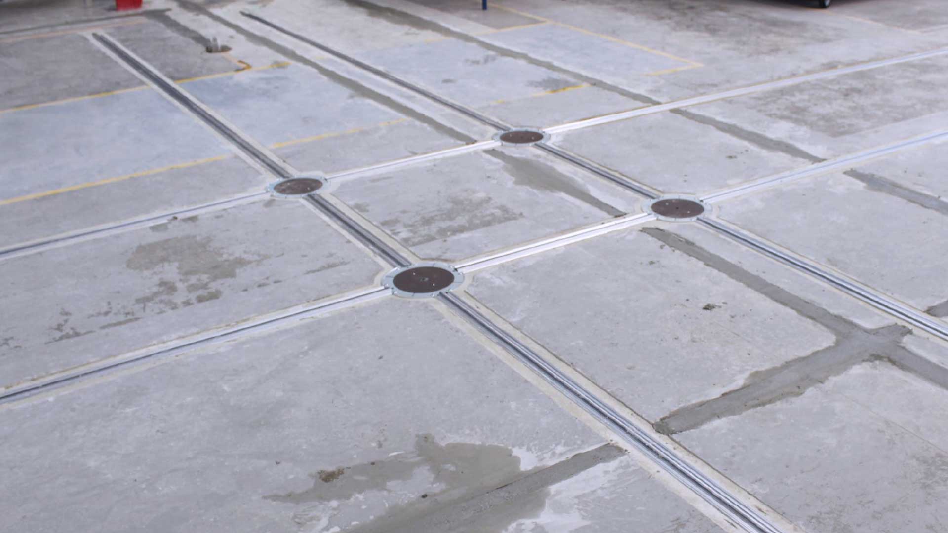 Boden eines Parkplatzes mit grauem Beton, markierten Linien und runden Abdeckungen in der Mitte von vier Kreuzungen.